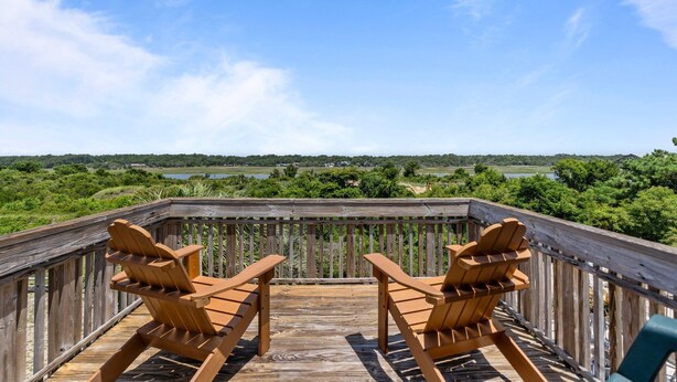 Une terrasse en bois avec deux fauteuils Adirondack donnant sur un paysage pittoresque composé d’un lac et d’une forêt.