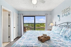 A bedroom with a bed, a nightstand, a lamp, and a view of the outdoors.