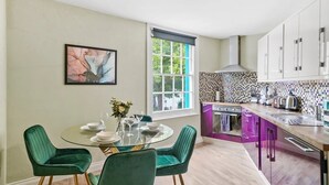 A modern kitchen with a dining area, featuring a round table with chairs, a window, and a colorful backsplash. - The Bristol Harbourside Apartments - Sleeps 16 (Bristol)