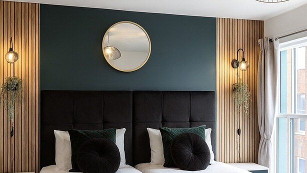 A double bed with dark green bedding, a round mirror above, and two wall-mounted lamps. - The Bristol Harbourside Apartments - Sleeps 16 (Bristol)