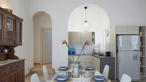Una cocina moderna con comedor, que incluye una mesa de vidrio, sillas blancas y una isla de cocina con refrigerador integrado.