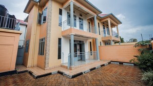 A two-story house with a balcony, a covered porch, and a brick driveway. - Casa Kigali (Kigali)