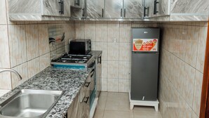 A compact kitchen with granite countertops, a gas stove, a microwave, and a refrigerator. - Casa Kigali (Kigali)