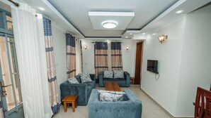 A living room with a blue sofa set, a wooden coffee table, and a TV mounted on the wall. - Casa Kigali (Kigali)