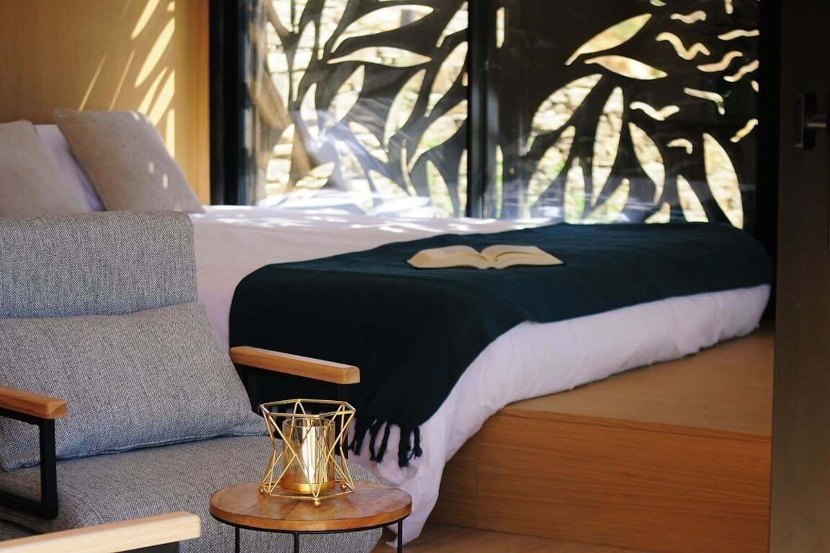 Un dormitorio acogedor con una cama, una silla y una mesita de noche con lámpara.