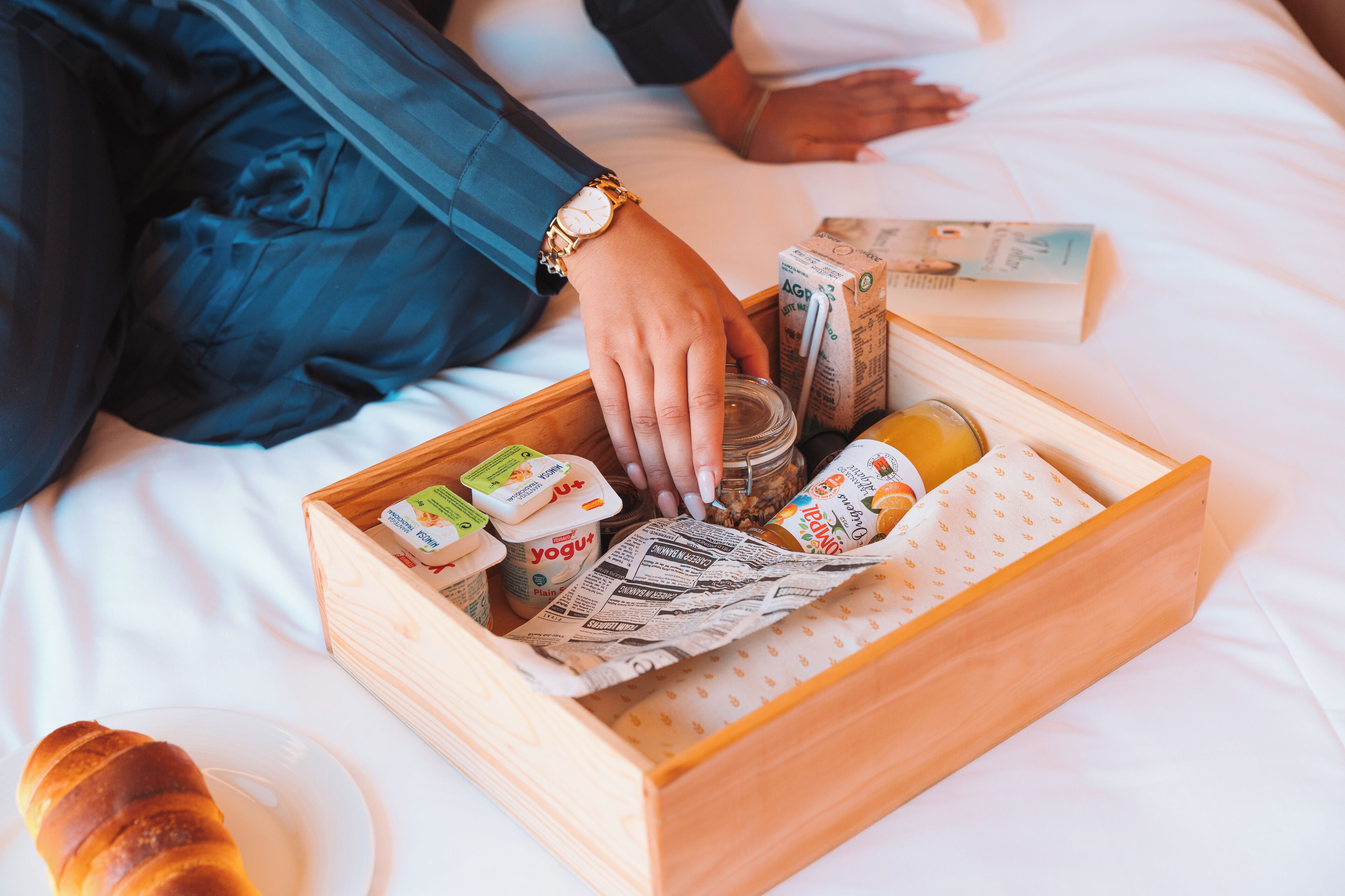 Una bandeja de madera con comida y un libro sobre la cama.