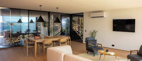 A modern living room with a dining area, large windows, and a view of the city.