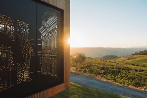A vineyard landscape with a river, a wooden fence, and a building with a black facade and white architectural drawings. - Five Sabrosa Senses (Sabrosa)