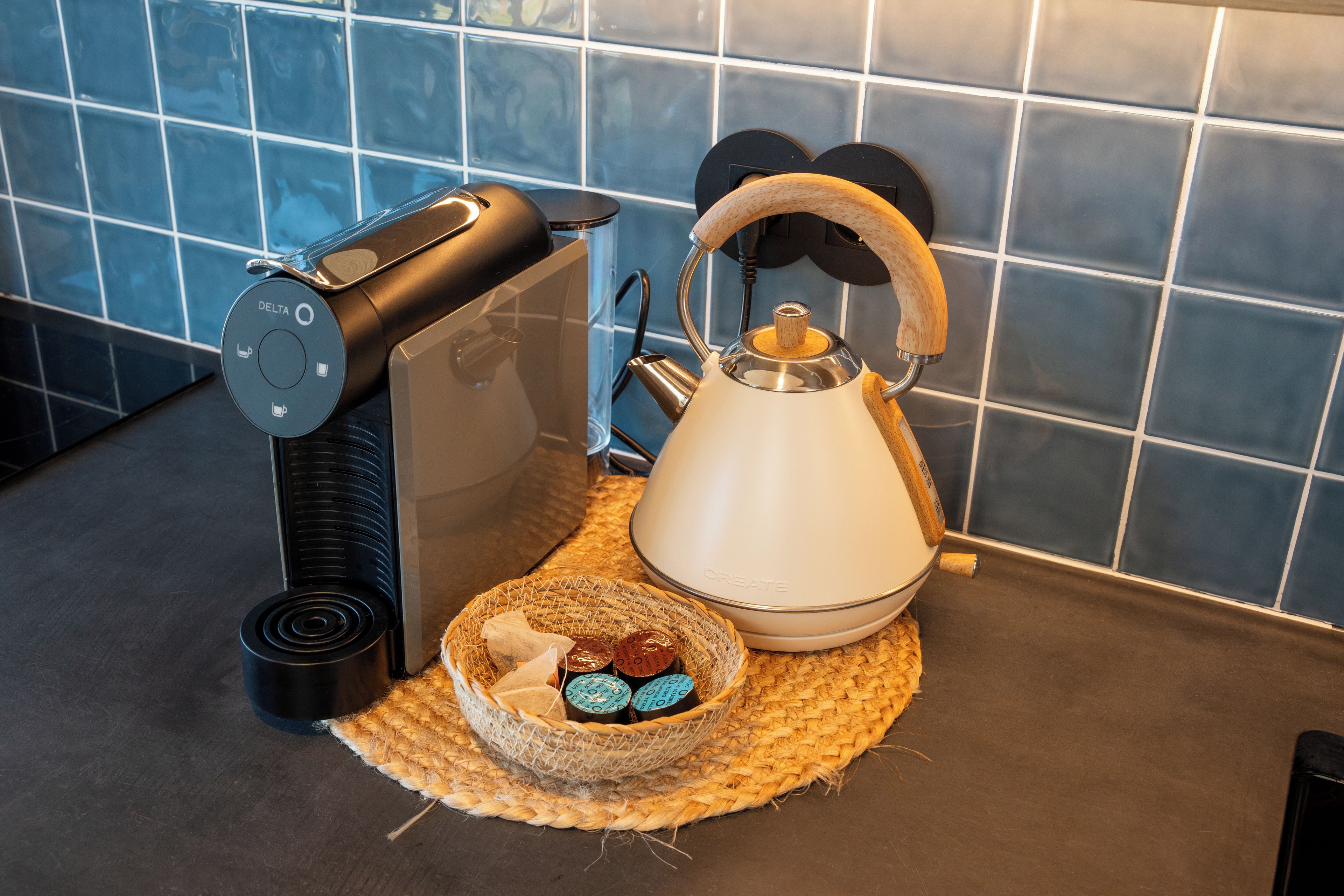 Cozinha com cafeteira, chaleira e um cesto com saquinhos de chá.