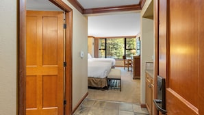 A hotel room with a wooden door, a bed, a desk, and a window with a view of trees. - Everline Queen Studio w/ Forest Views # 723 (Olympic Valley)