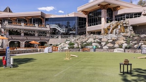 A hotel with a modern architectural style, featuring a large glass facade, outdoor seating area with orange umbrellas, and a landscaped garden with a small waterfall. - Everline Queen Studio w/ Forest Views # 723 (Olympic Valley)