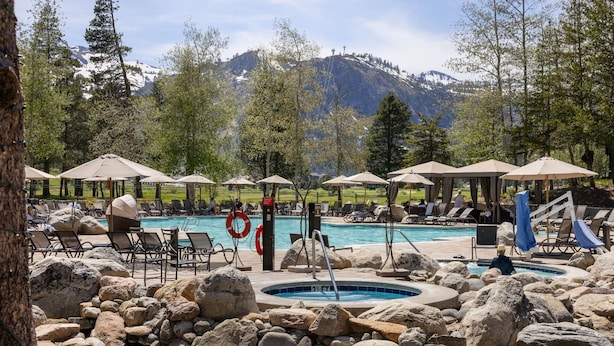 A pool area with lounge chairs, umbrellas, and a hot tub surrounded by rocks. - Everline Queen Studio w/ Forest Views # 723 (Olympic Valley)
