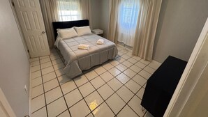 A bedroom with a bed, curtains, a ceiling fan, and a tiled floor.