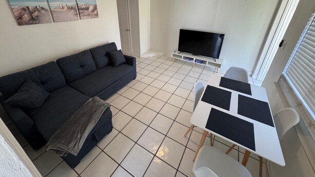 A living room with a dark sofa, a TV, a dining table with chairs, and a ceiling fan.