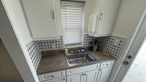 A small kitchen with white cabinets, a granite countertop, a stainless steel sink, and a window with blinds.