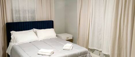 A neatly made bed with white linens, a dark blue headboard, and a bedside table with a drawer.