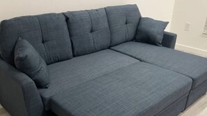 A grey sectional sofa with a chaise, a small table, and a light-colored tiled floor.