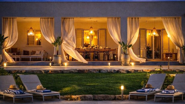 A modern outdoor dining area with a pool, lounge chairs, and a well-lit patio.