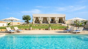 A poolside area with lounge chairs and umbrellas, a pool, and a building with a covered patio.