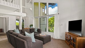 Un salón espacioso con un sofá modular, un mueble de entretenimiento de madera y grandes ventanales con vistas al exterior.