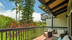 Terraza de madera con mobiliario de mimbre y vistas a un jardín exuberante y altos árboles.