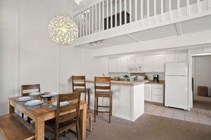 Une cuisine moderne avec des meubles blancs, un îlot central et un coin repas comprenant des chaises et une table en bois.