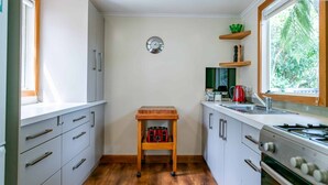 Une cuisine de taille réduite avec des meubles blancs, une table en bois, un grille-pain rouge, un évier et une fenêtre donnant sur un paysage verdoyant.