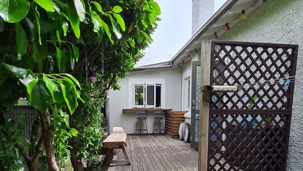 Une terrasse en bois avec des marches menant à l’entrée de la maison, entourée de verdure et agrémentée d’une porte à treillis.