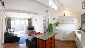 Un appartement moderne comprenant un salon, une cuisine et un coin repas. Il est doté d’une grande fenêtre, d’un téléviseur à écran plat, d’une table à manger et d’une cuisine avec des meubles blancs.