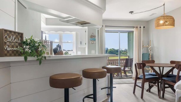 Une cuisine moderne avec des meubles blancs, un coin bar avec des tabourets et un ensemble de salle à manger comprenant des chaises et une table.