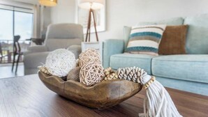 Un saladier en bois sur une table, agrémenté d’objets décoratifs, un canapé bleu clair, une lampe et une chaise dans un salon moderne.