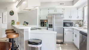 Une cuisine moderne avec des meubles blancs, des appareils en acier inoxydable et un îlot central doté de tabourets.