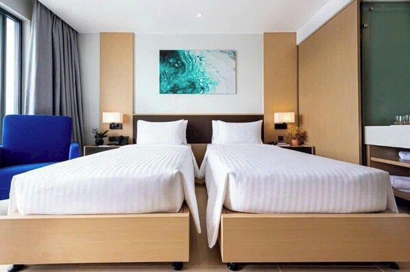 A hotel room with two beds, a blue chair, a painting on the wall, and a large window with curtains. - Arena Jakovi Condotel (Bac Cam Ranh)