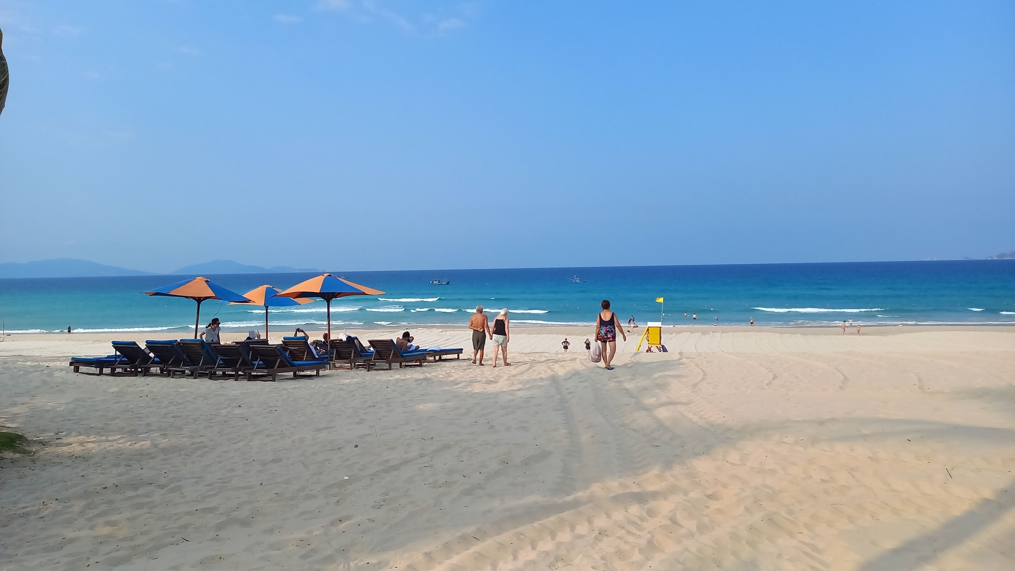Una playa con tumbonas y sombrillas, un puesto de socorrista y el océano.