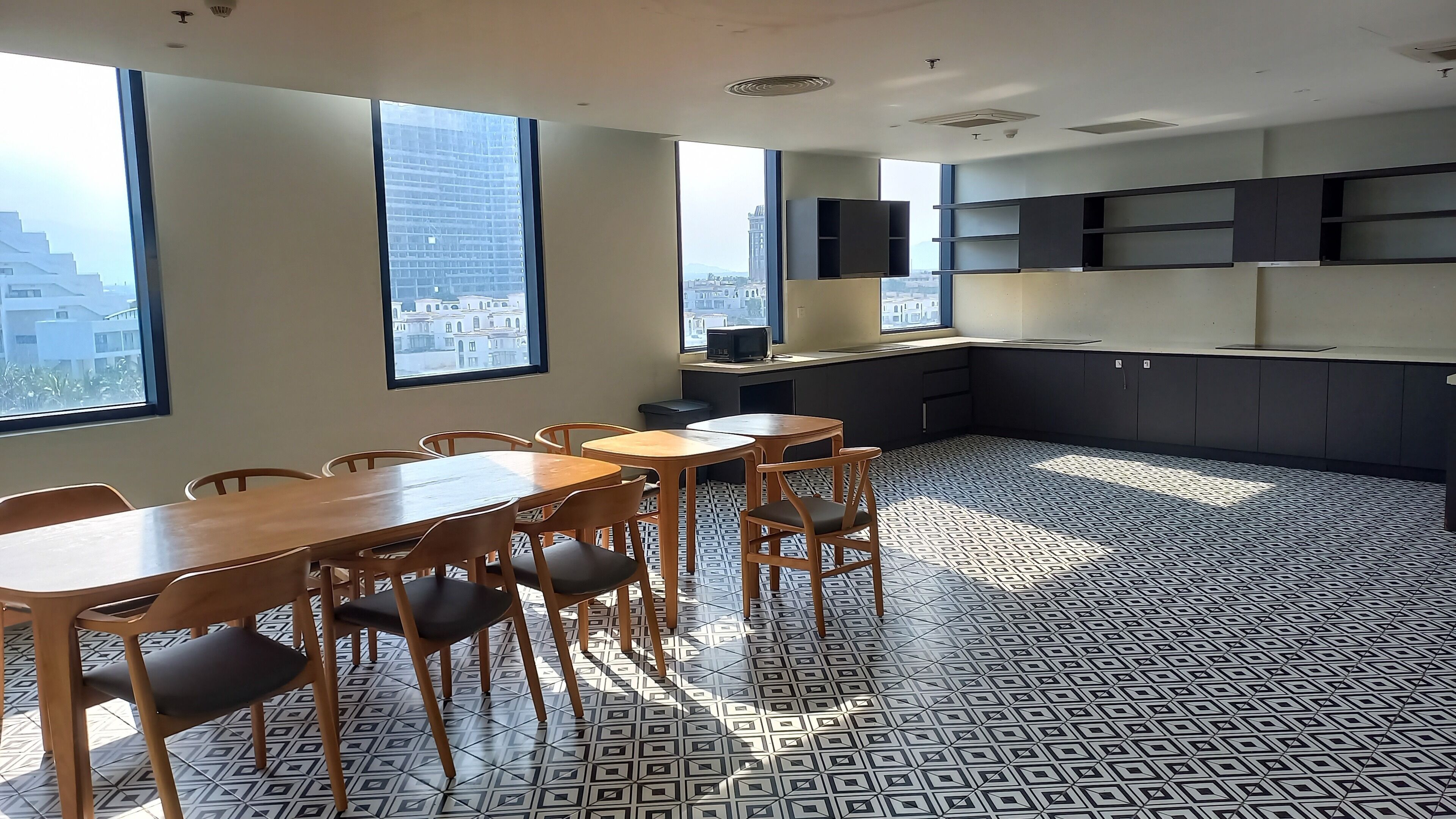 A modern kitchen with large windows, a dining area with wooden tables and chairs, and a patterned floor.