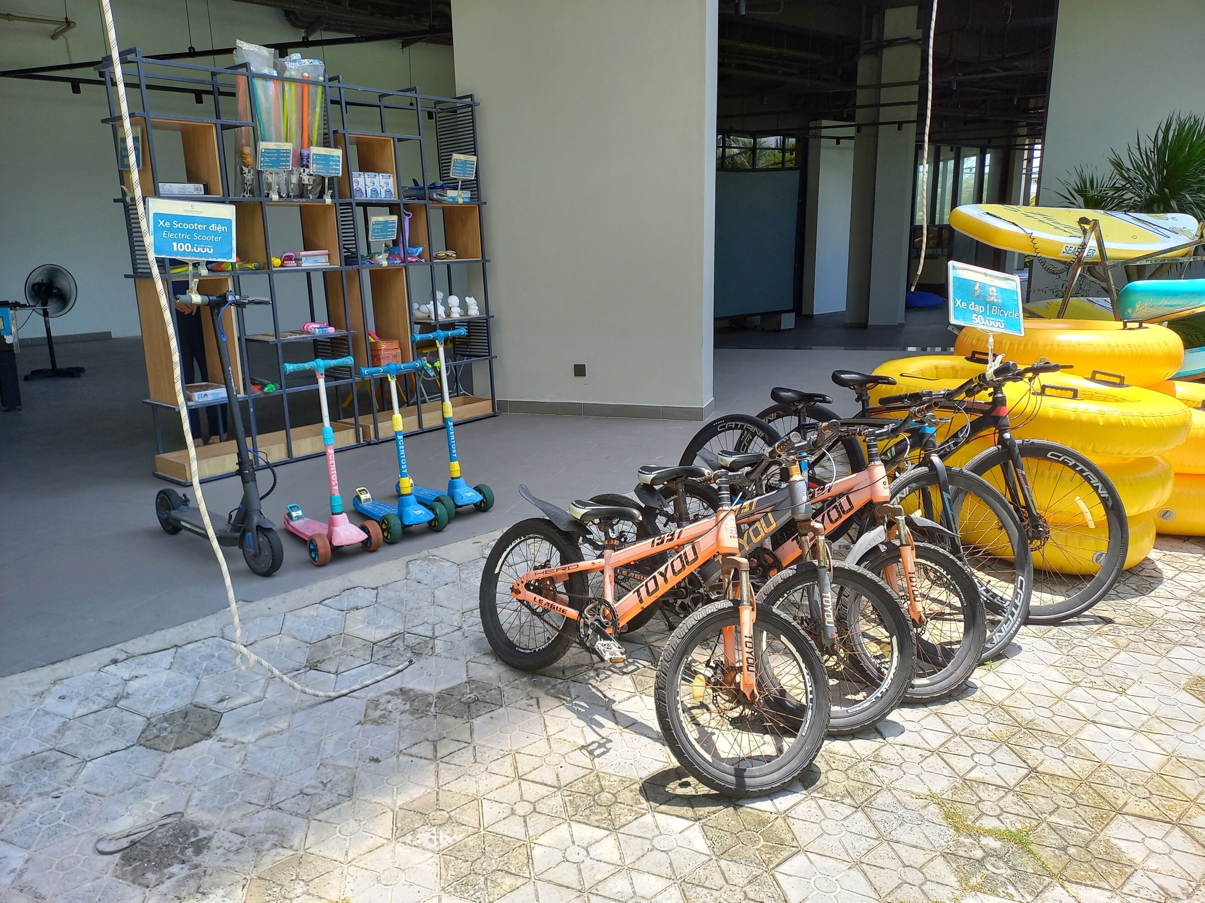 Uma área de estacionamento com bicicletas e scooters, um ventilador e uma exposição de scooters elétricas.