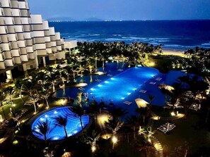 A resort with a large swimming pool, palm trees, and a view of the ocean. - Arena Jakovi Condotel (Bac Cam Ranh)