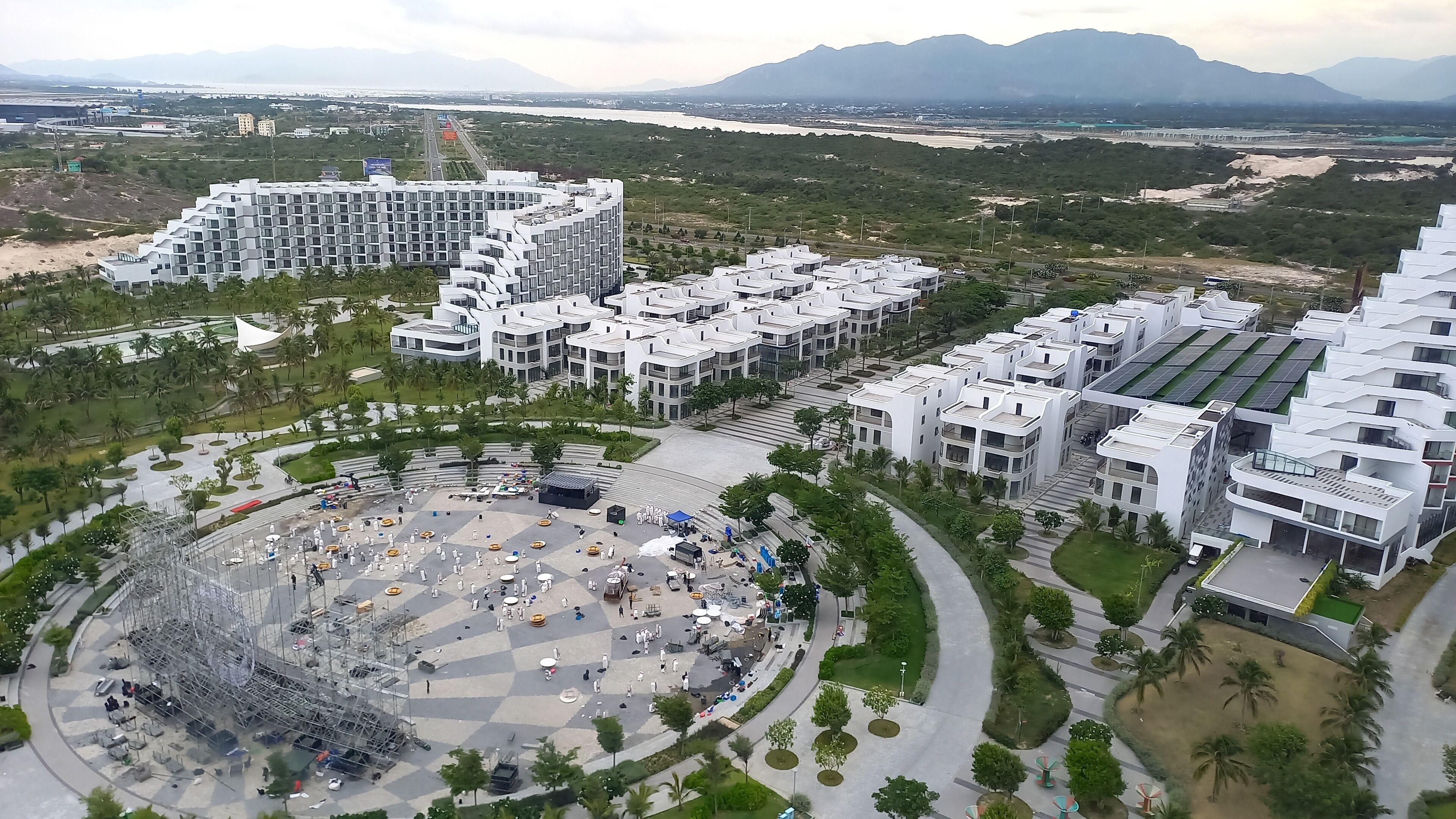 Un complex residencial modern amb diversos edificis, un espai central obert amb seients i una vista d'un aeroport i muntanyes a la distància.