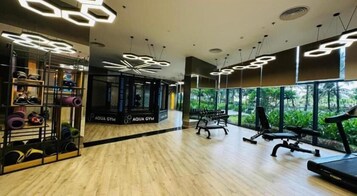 Un gimnasio con suelo de madera, equipo de ejercicio e iluminación con focos hexagonales.