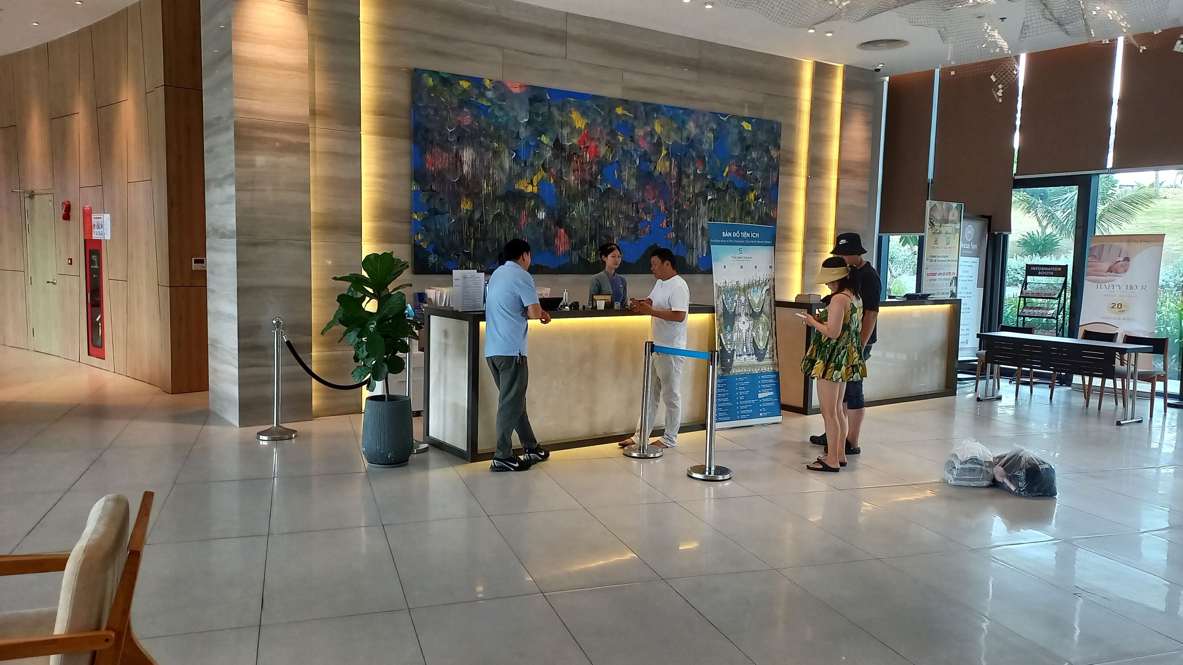 A hotel reception area with a modern design, a reception desk, a large abstract painting, and a seating area with tables and chairs.