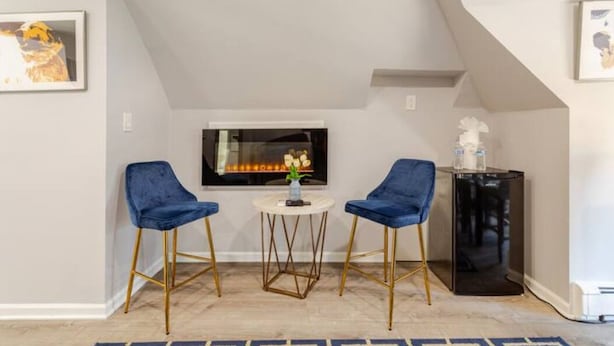 Una habitación acogedora con chimenea, dos sillones azules, una mesita redonda y un armario negro.