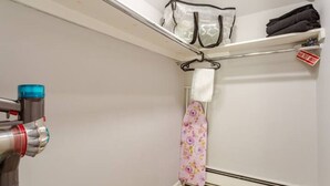 Una habitación pequeña y estrecha con tabla de planchar integrada, perchero y calefactor.