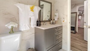 Un baño con pared de mármol, lavamanos, espejo y retrete.
