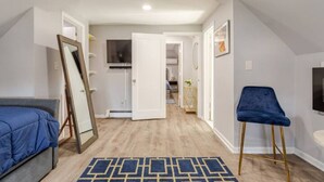 Un dormitorio moderno con cama, una silla azul, un espejo y televisor en la pared.