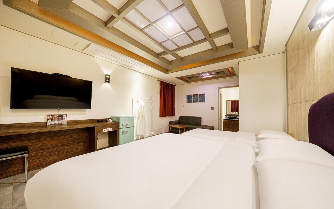 A hotel room with a large bed, a flat-screen TV mounted on the wall, a desk with a chair, and a small table.