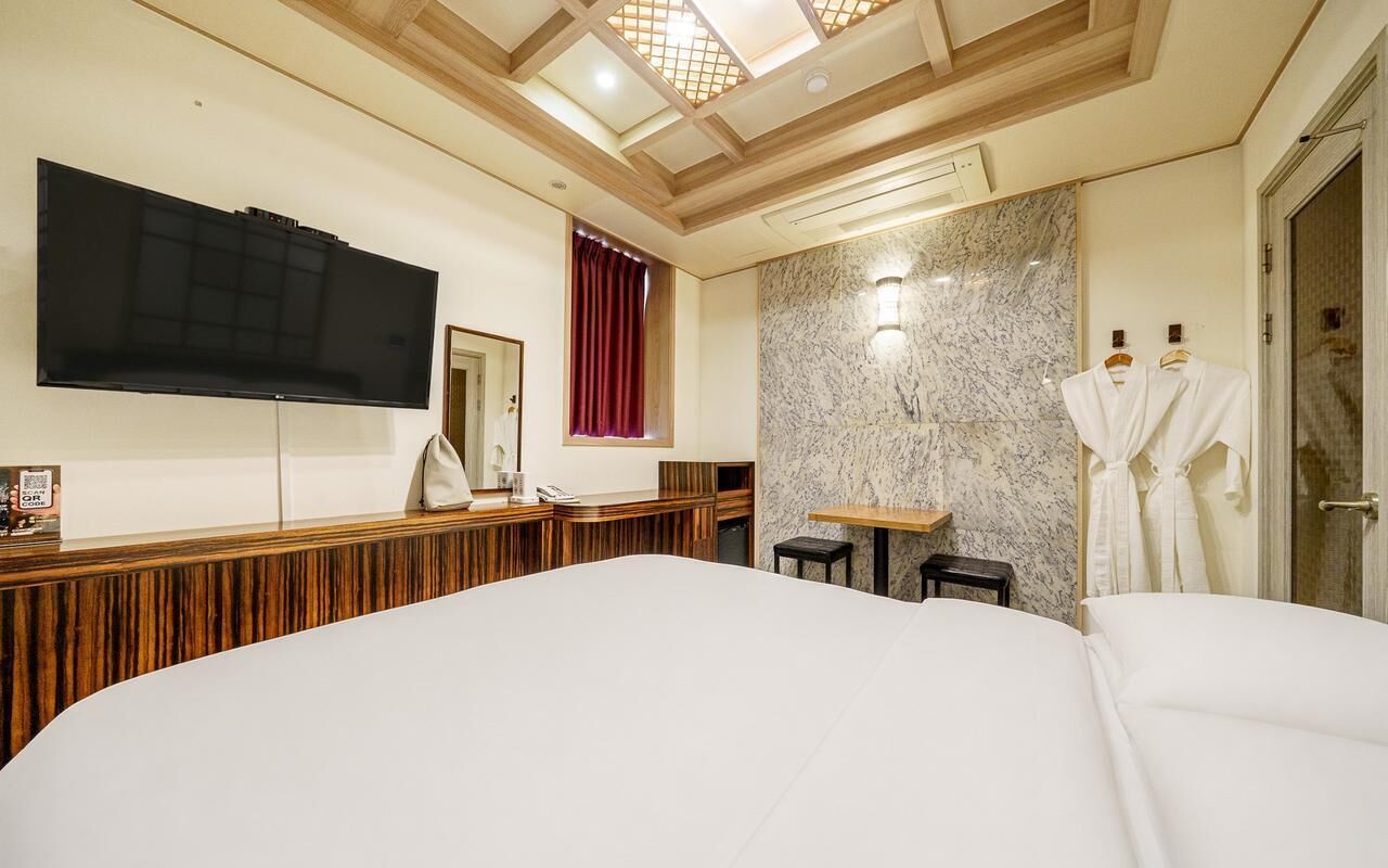 A hotel room with a large bed, a television mounted on the wall, a small table, and a mirror.