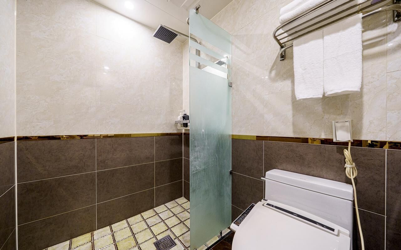 A bathroom with a glass shower door, a white toilet, and a towel rack with towels.
