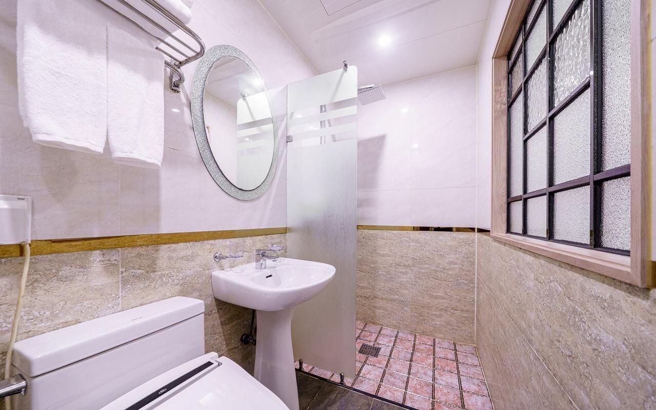 A bathroom with a toilet, sink, mirror, and window.