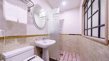 A bathroom with a toilet, sink, mirror, and window.