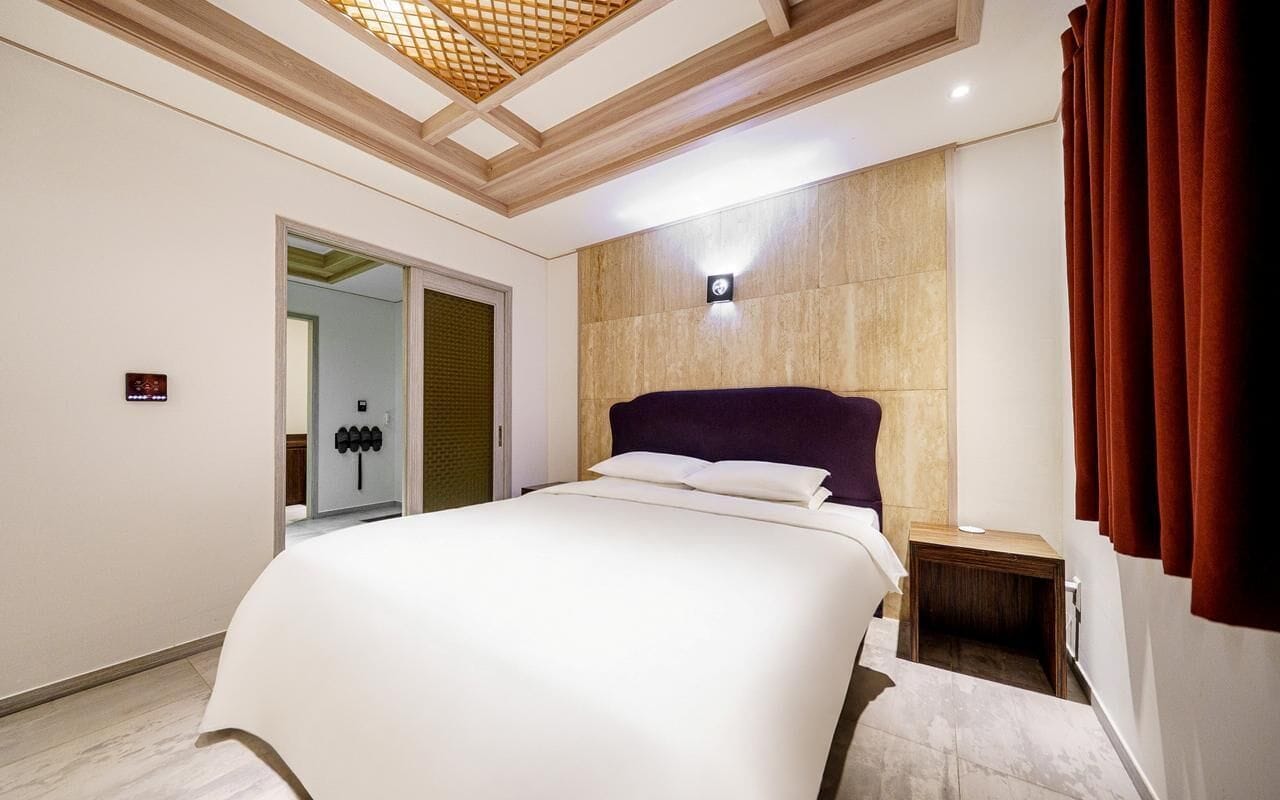 A modern hotel room with a large bed, a wooden headboard, a nightstand, and a mirror.